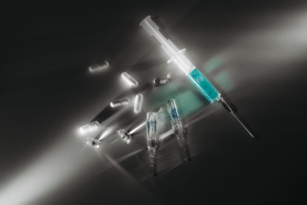 Syringe and medicine capsules illuminated in a dark, dramatic setting, emphasizing medical themes.